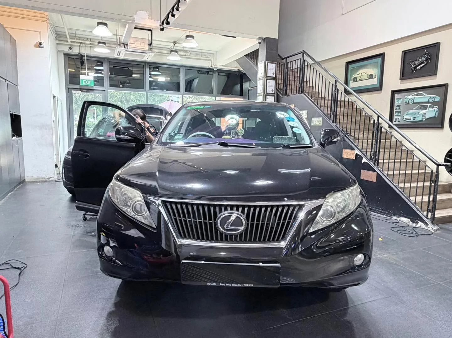 A black Lexus SUV with distinctive spindle grille, parked indoors with doors open.