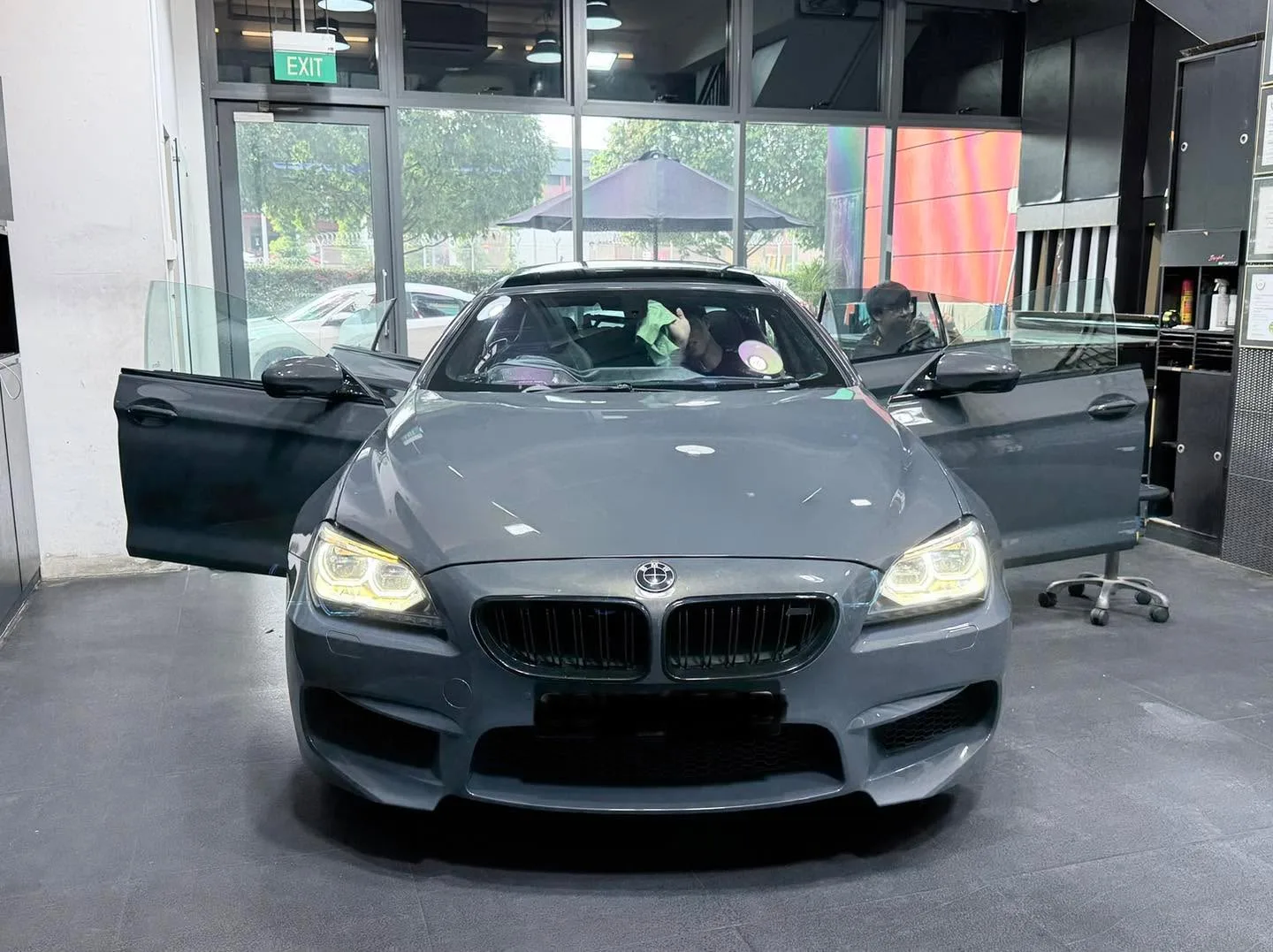 A grey BMW coupe with doors open, parked indoors.