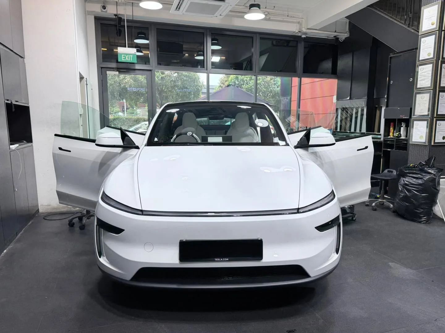 A white Tesla sedan with doors raised, viewed from above indoors.