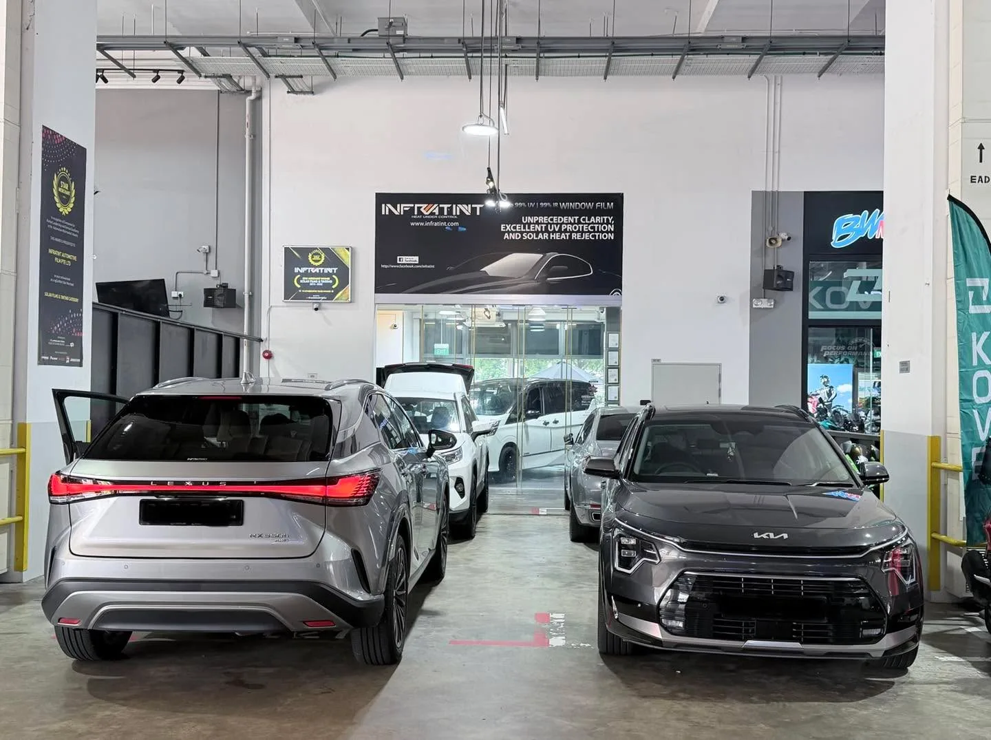 A silver Toyota RAV4 and black Kia Niro in a workshop bay with Infratint signage visible.