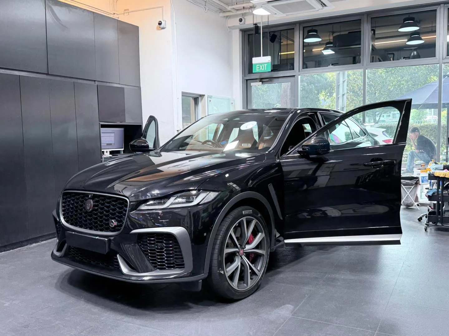 A black Jaguar F-Pace SVR with driver door open inside a workshop bay.