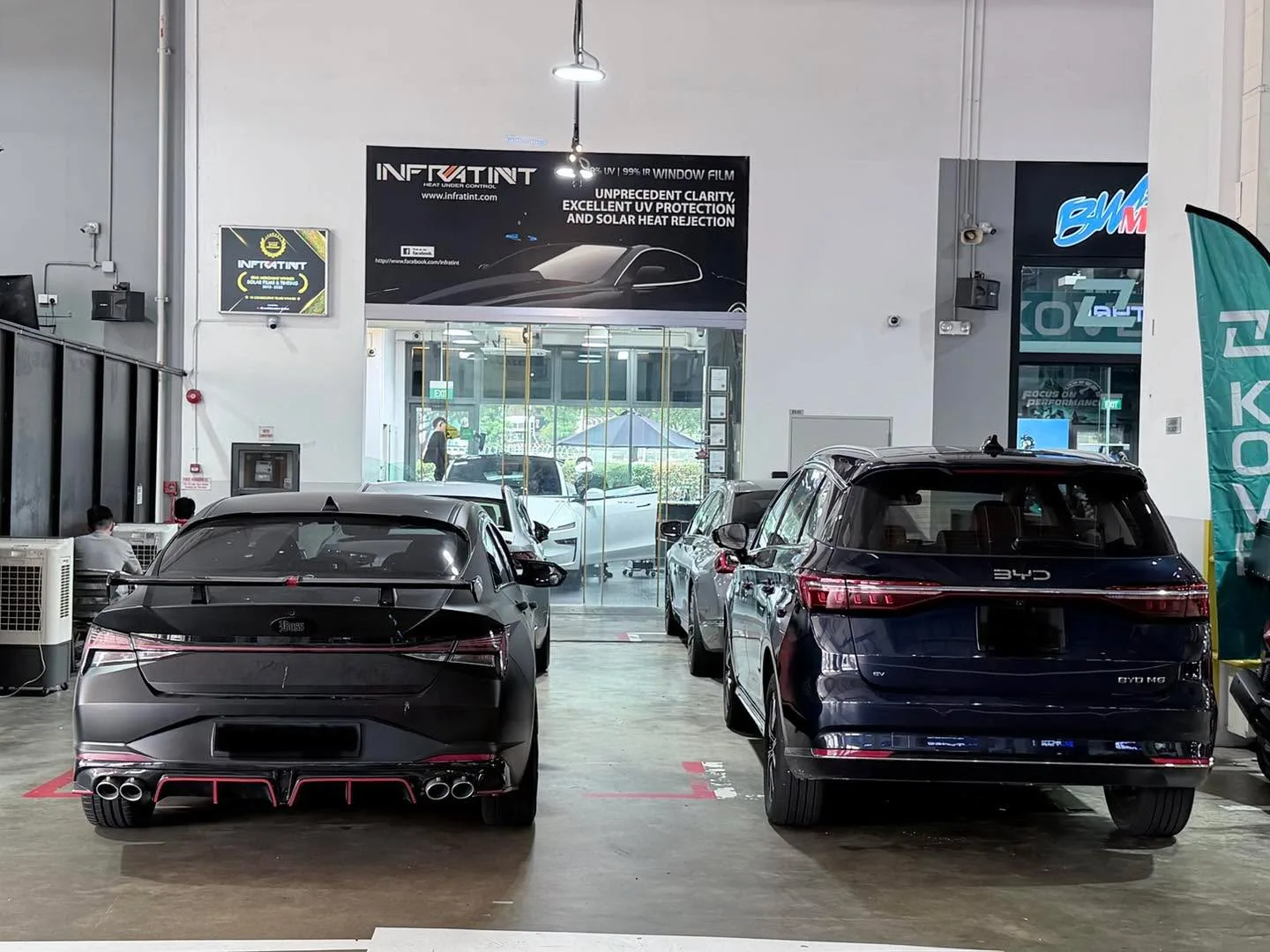 A black sports car with quad exhaust pipes and a silver BYD SUV parked in a workshop.