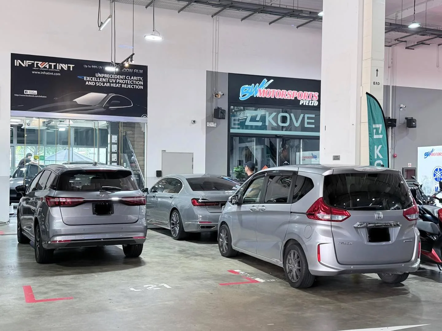 A silver BYD SUV and two silver hatchbacks parked in a workshop.