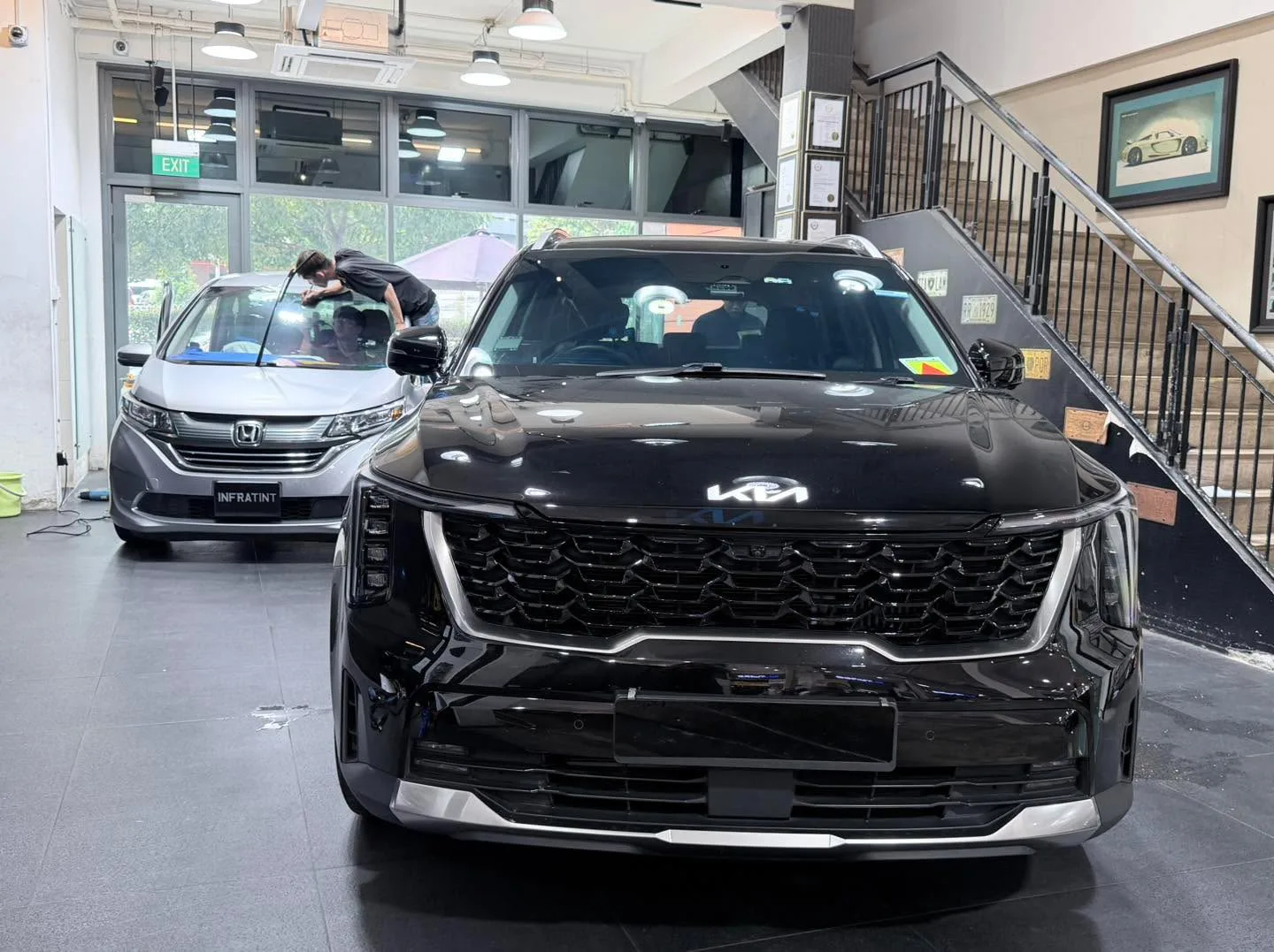 A black Kia Sorento SUV and a white Honda Freed minivan being tinted in the workshop.