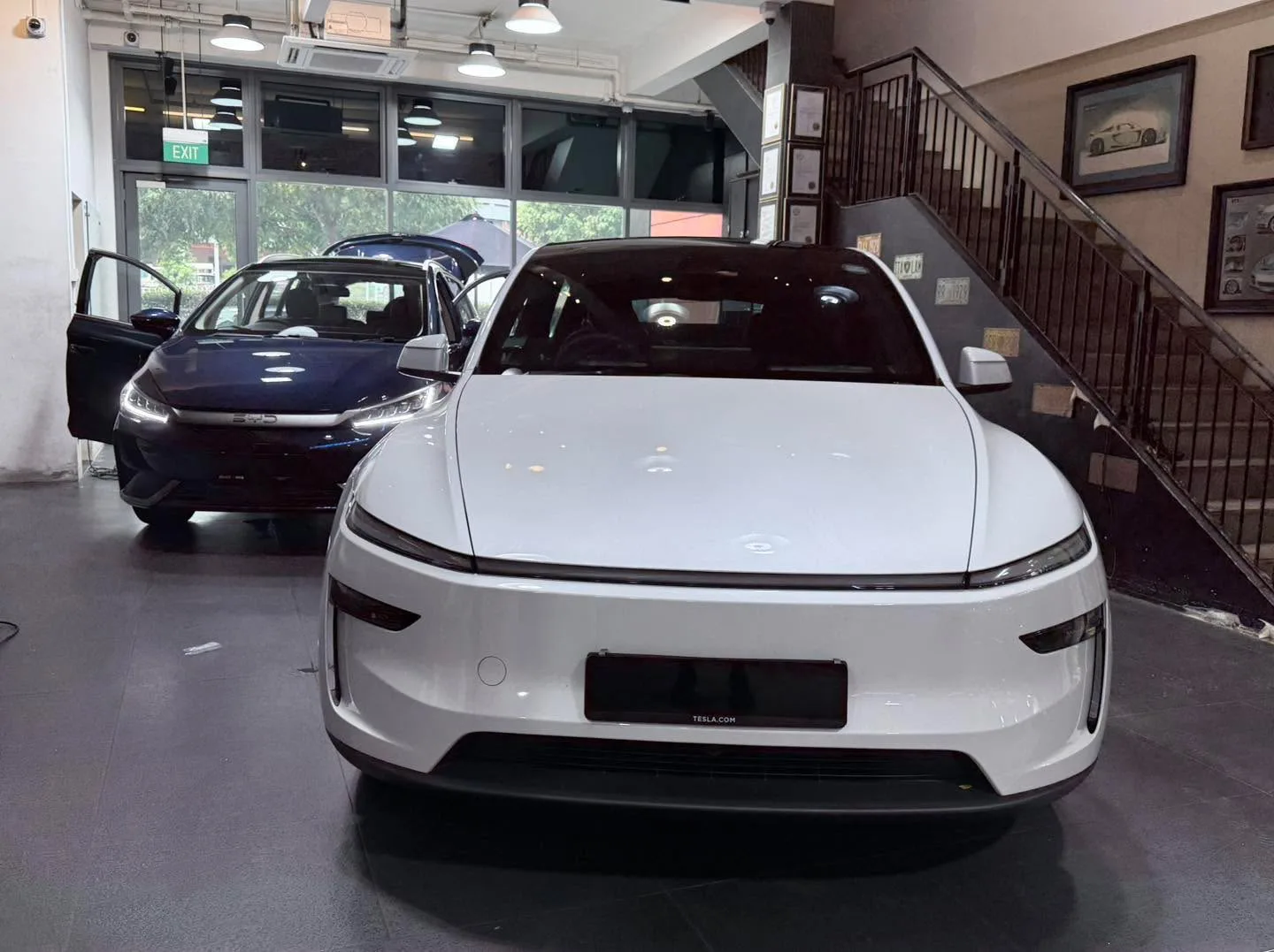 A white Tesla sedan and a dark-coloured sedan parked in the workshop.