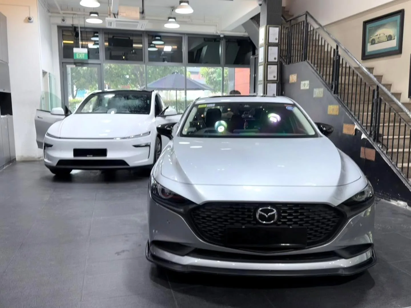 A white Tesla sedan and a white Mazda 3 hatchback parked in the workshop.