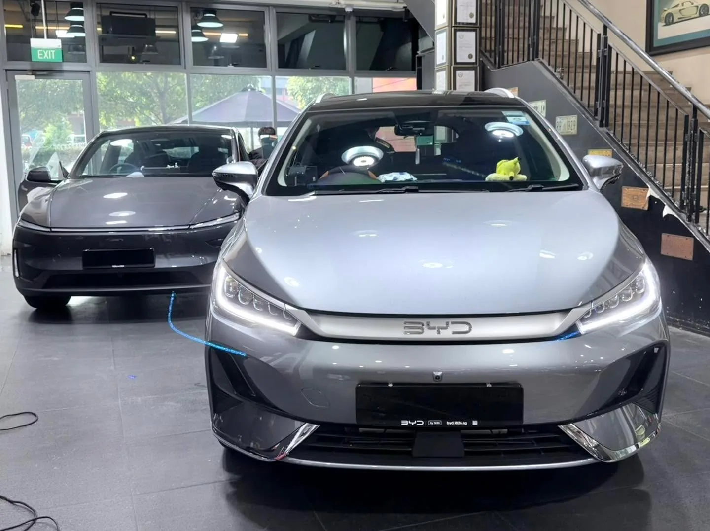 A silver Mazda 3 hatchback and a white Tesla sedan parked in the workshop.