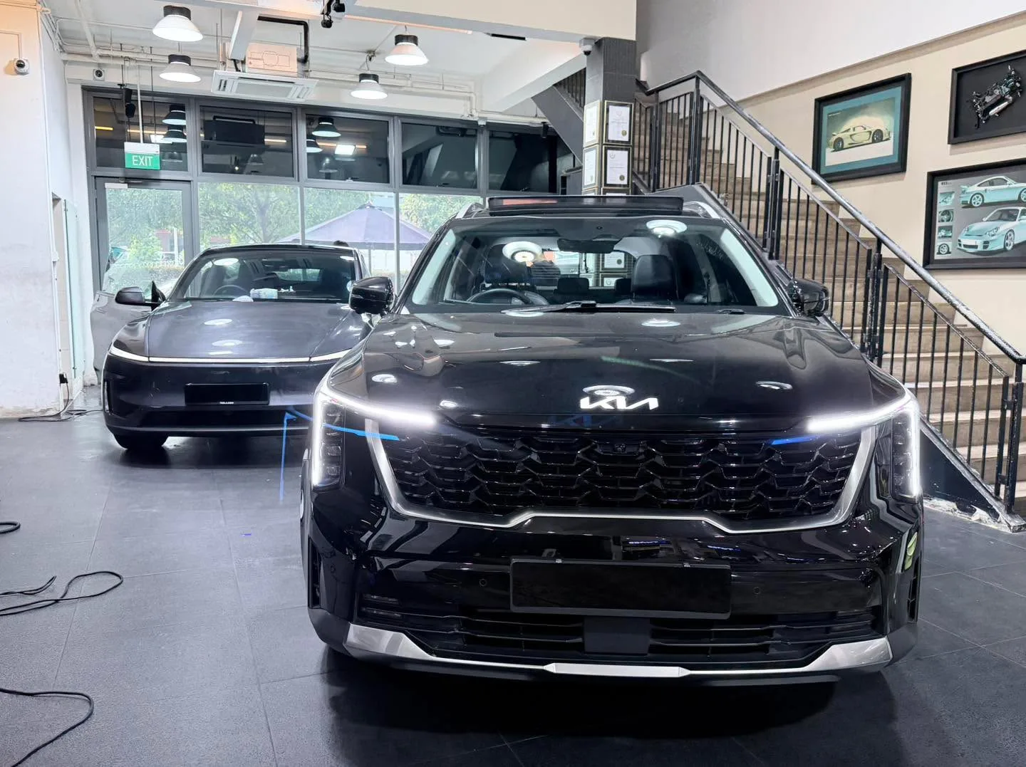A black Kia Sorento SUV and a dark-coloured sedan parked in the workshop.