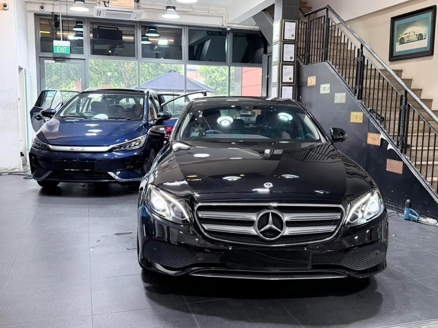 A blue Hyundai Avante sedan and a black Mercedes-Benz sedan parked in the workshop.
