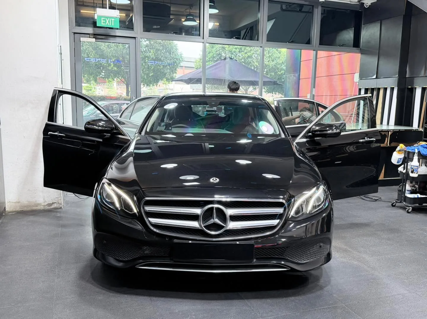 A black Mercedes-Benz E-Class sedan with both doors open in the workshop.