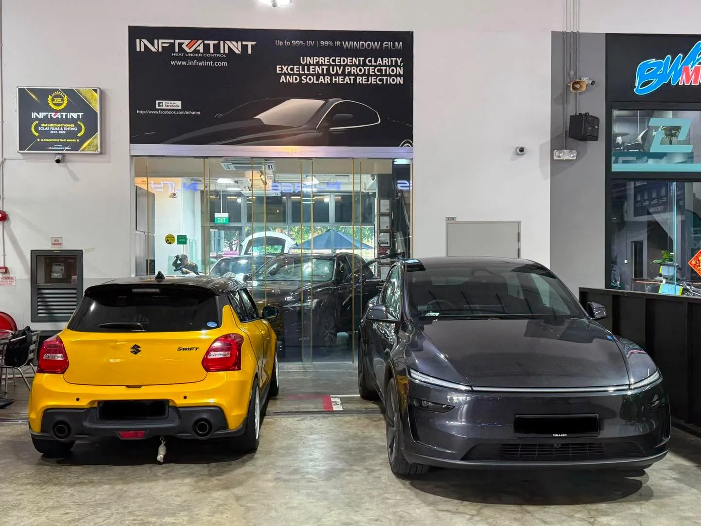 Yellow Suzuki Swift and dark grey sedan parked outside workshop.