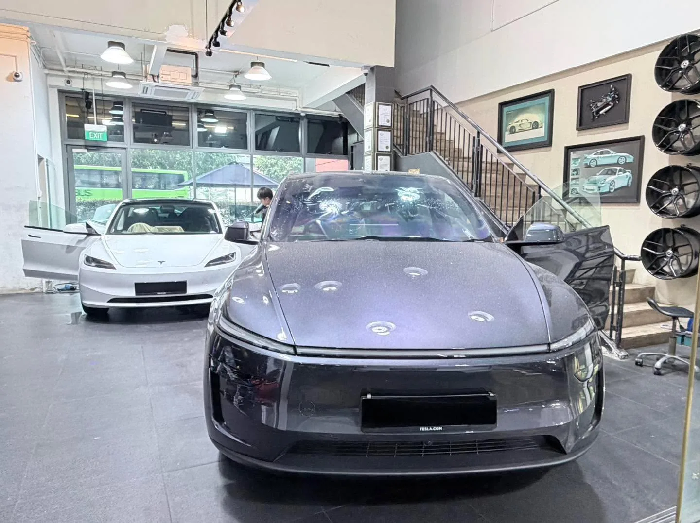 Dark grey Tesla saloon being tinted indoors, white Tesla visible behind.