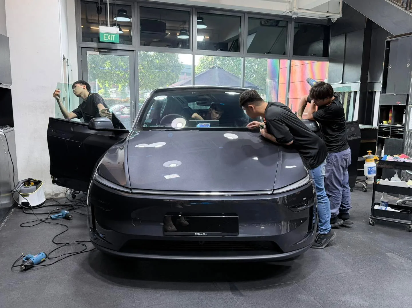 Dark grey Tesla being tinted by three technicians working on windows.