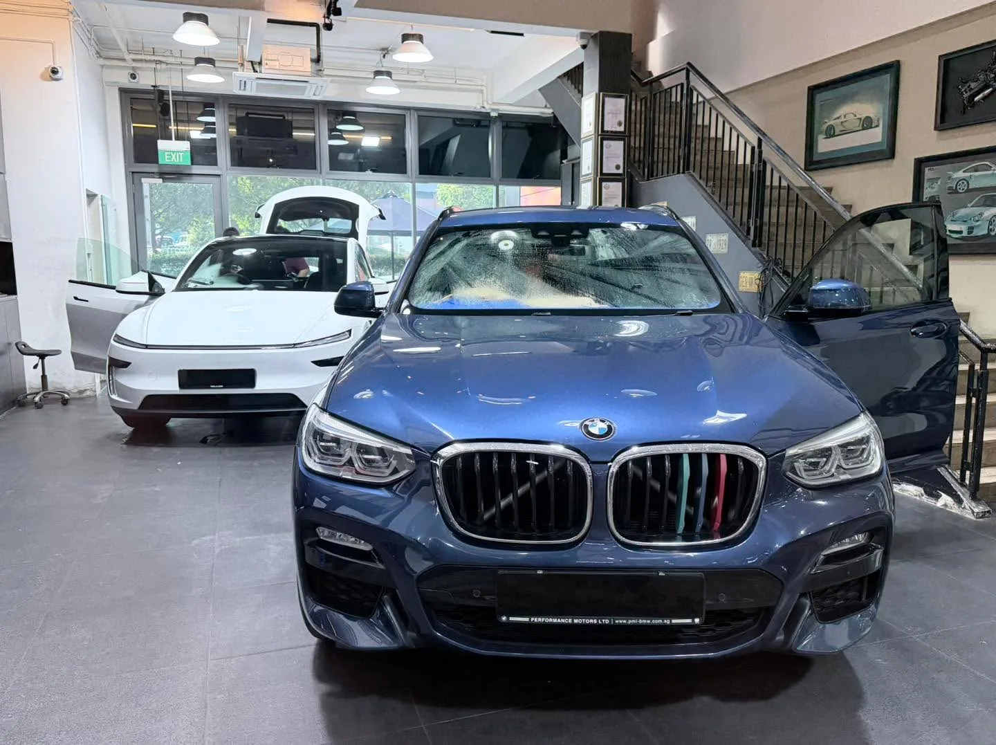 A blue BMW saloon viewed from the front, with a white Tesla behind it.