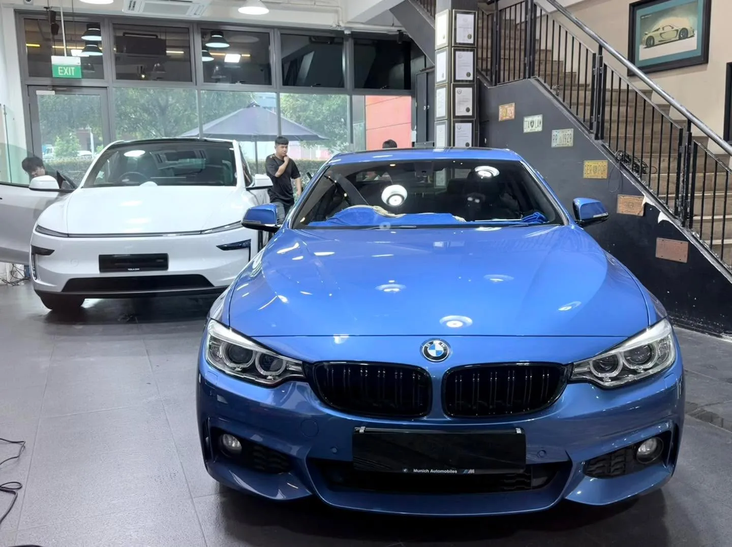 A blue BMW saloon viewed from the front, with a white car behind.