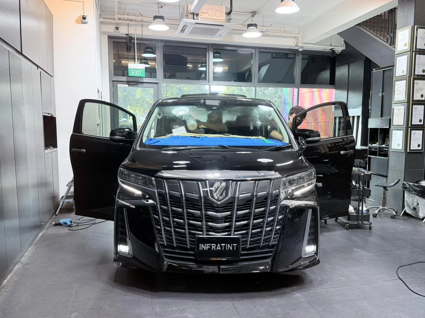 A black Toyota Alphard with doors open, positioned centrally in the workshop.