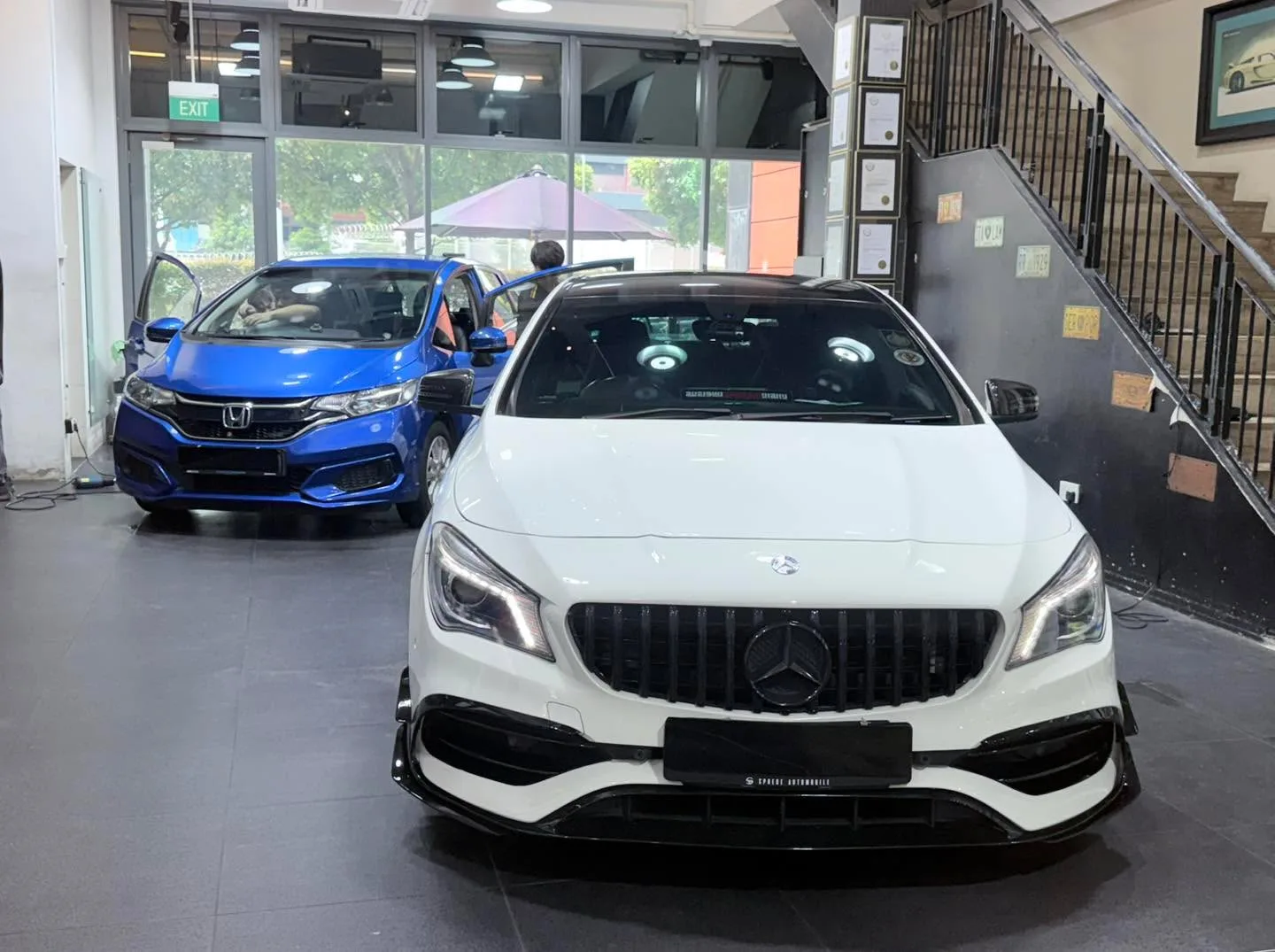 A white Mercedes-Benz saloon with AMG grille, viewed from the front, with a blue Honda to the left.