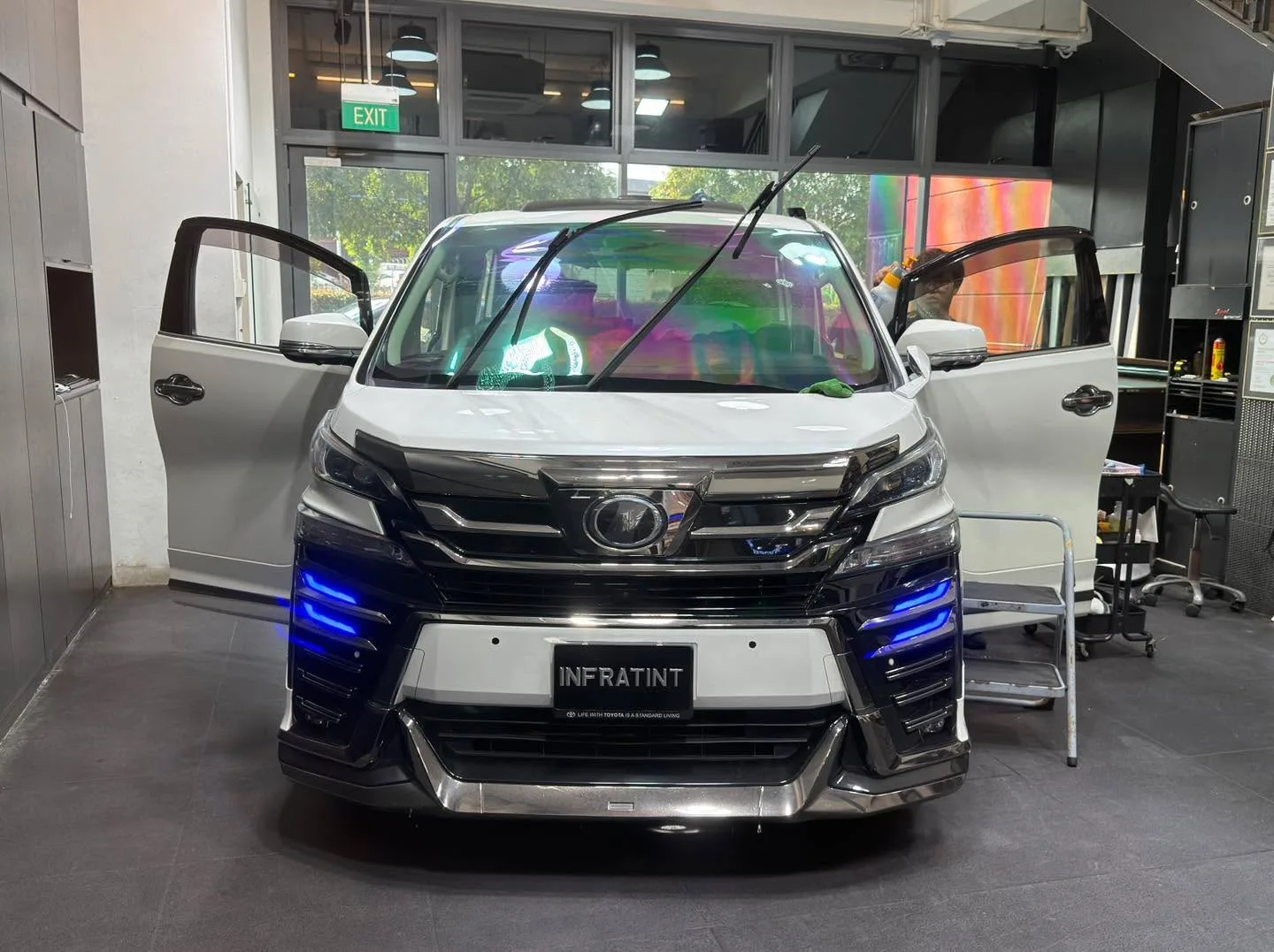 A black and white Toyota MPV with its doors open, technician working on the driver side window.