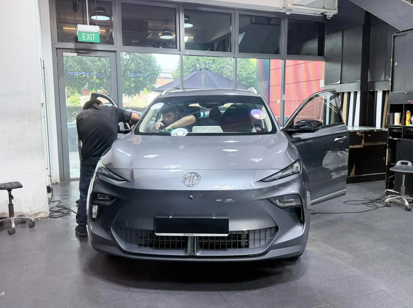 A silver saloon with driver door open, technician applying window film.