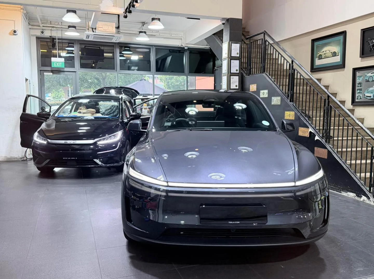 A black Tesla sedan with doors open and a dark grey Tesla sedan in the foreground, in the workshop.