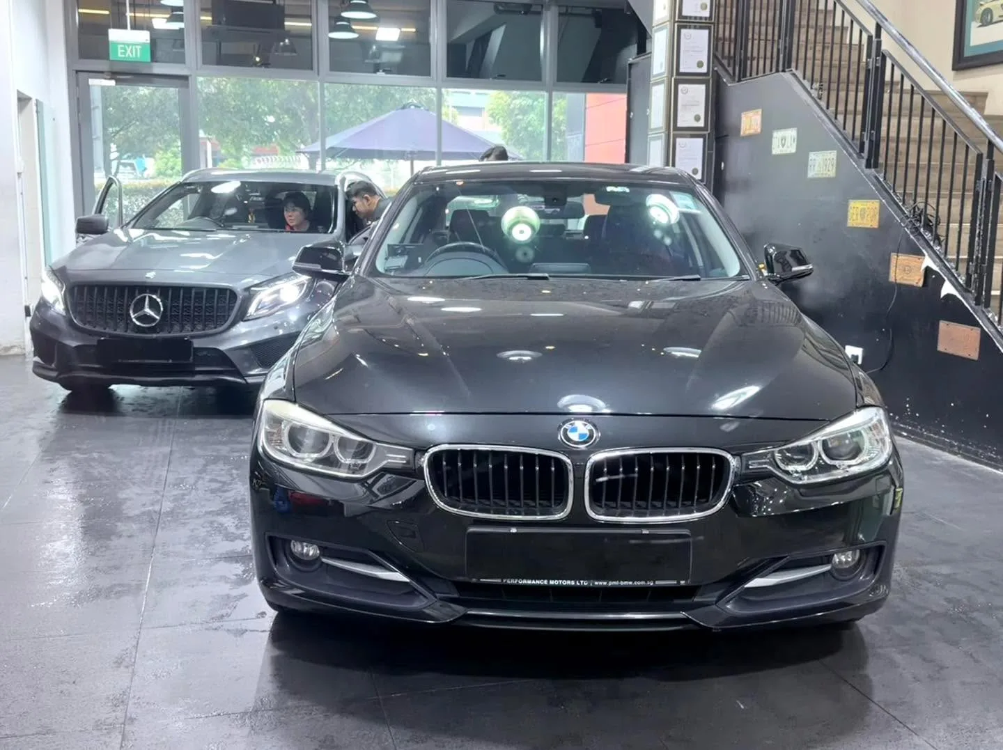 A black BMW saloon in the foreground and a grey Mercedes-Benz compact SUV behind it, in the workshop.