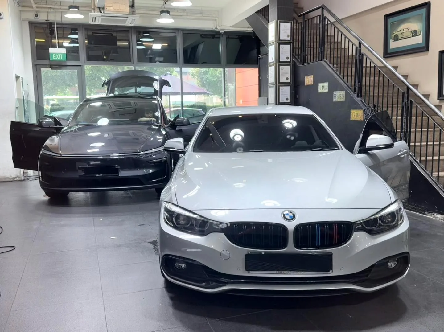 A white BMW saloon in the foreground, doors open, and a black Tesla sedan behind it.