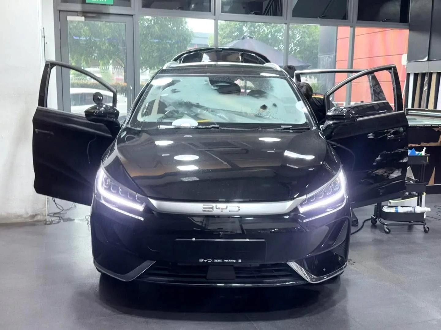 A dark-coloured BYD compact sedan with both doors open, in the workshop.
