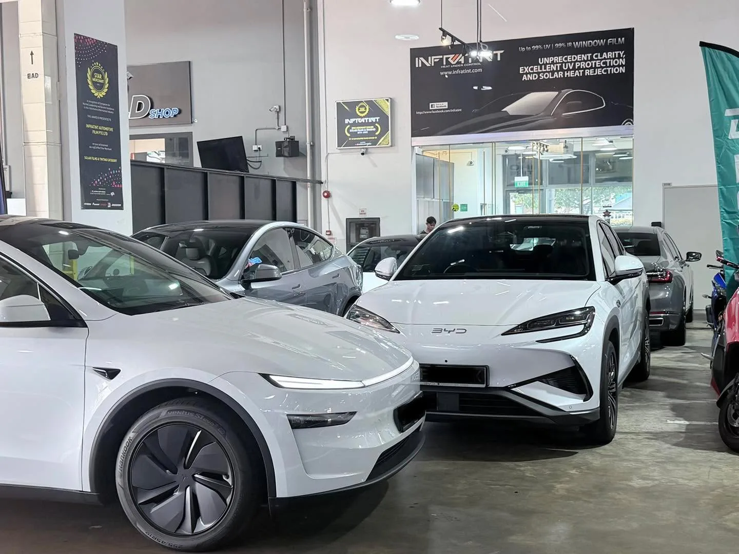 White Tesla Model Y and grey Tesla Model 3 parked indoors at the workshop.