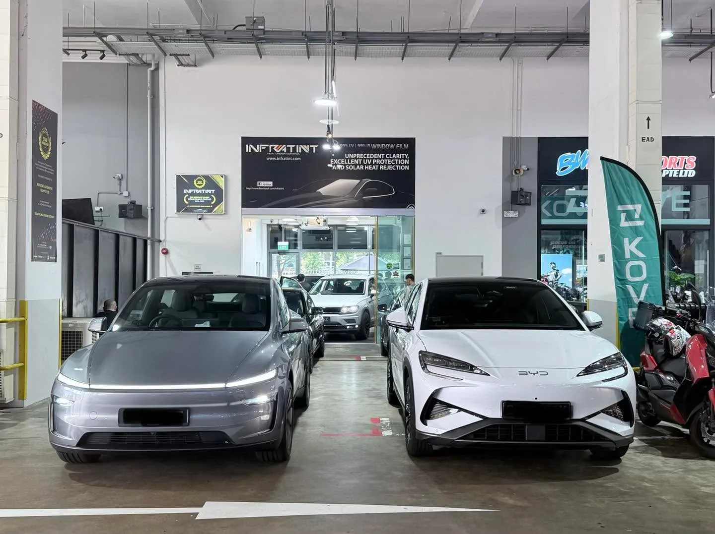 Silver Tesla Model Y and white Tesla Model Y parked facing each other indoors.