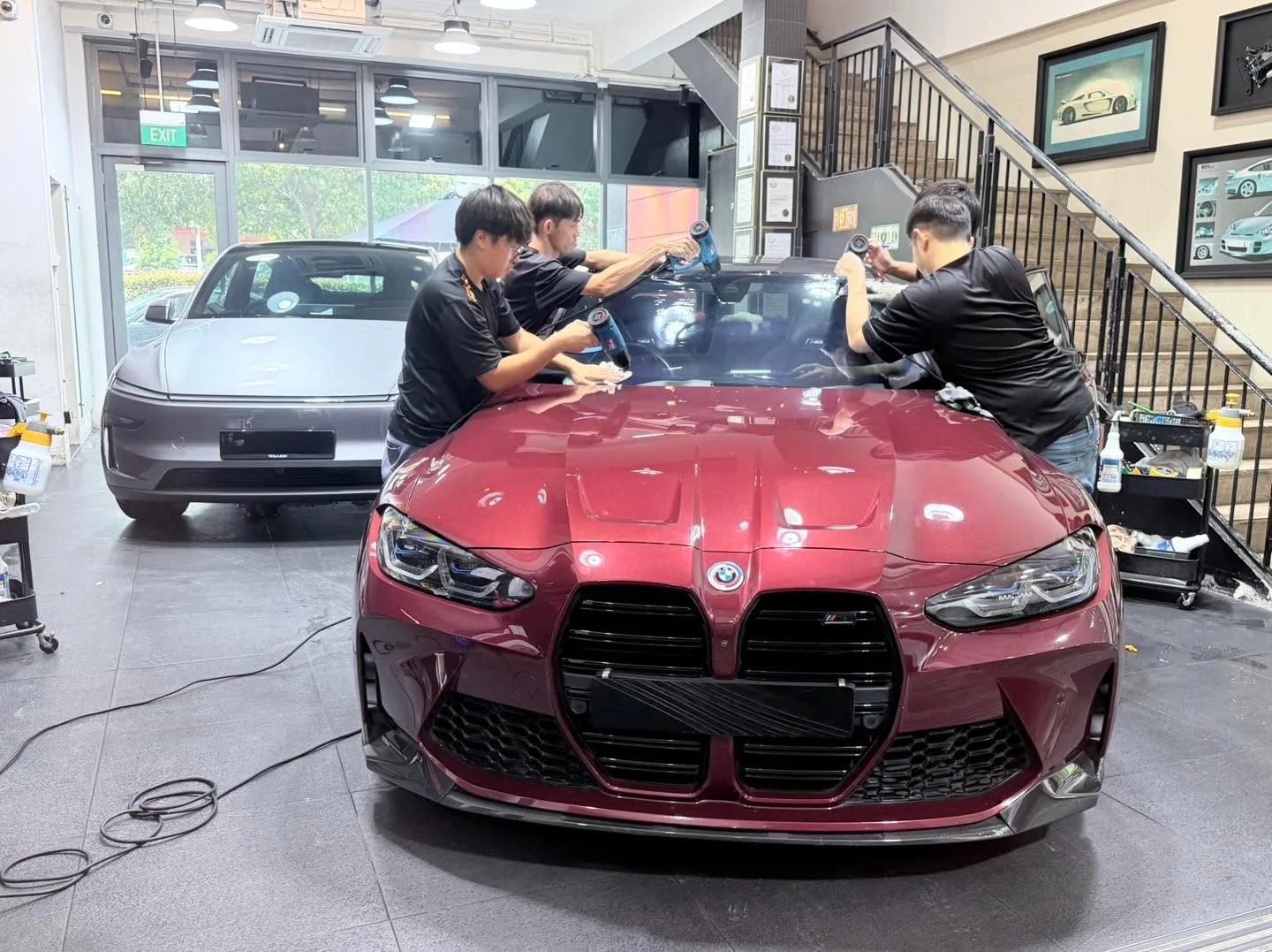 Red BMW M3 with doors open, technicians applying window tint.