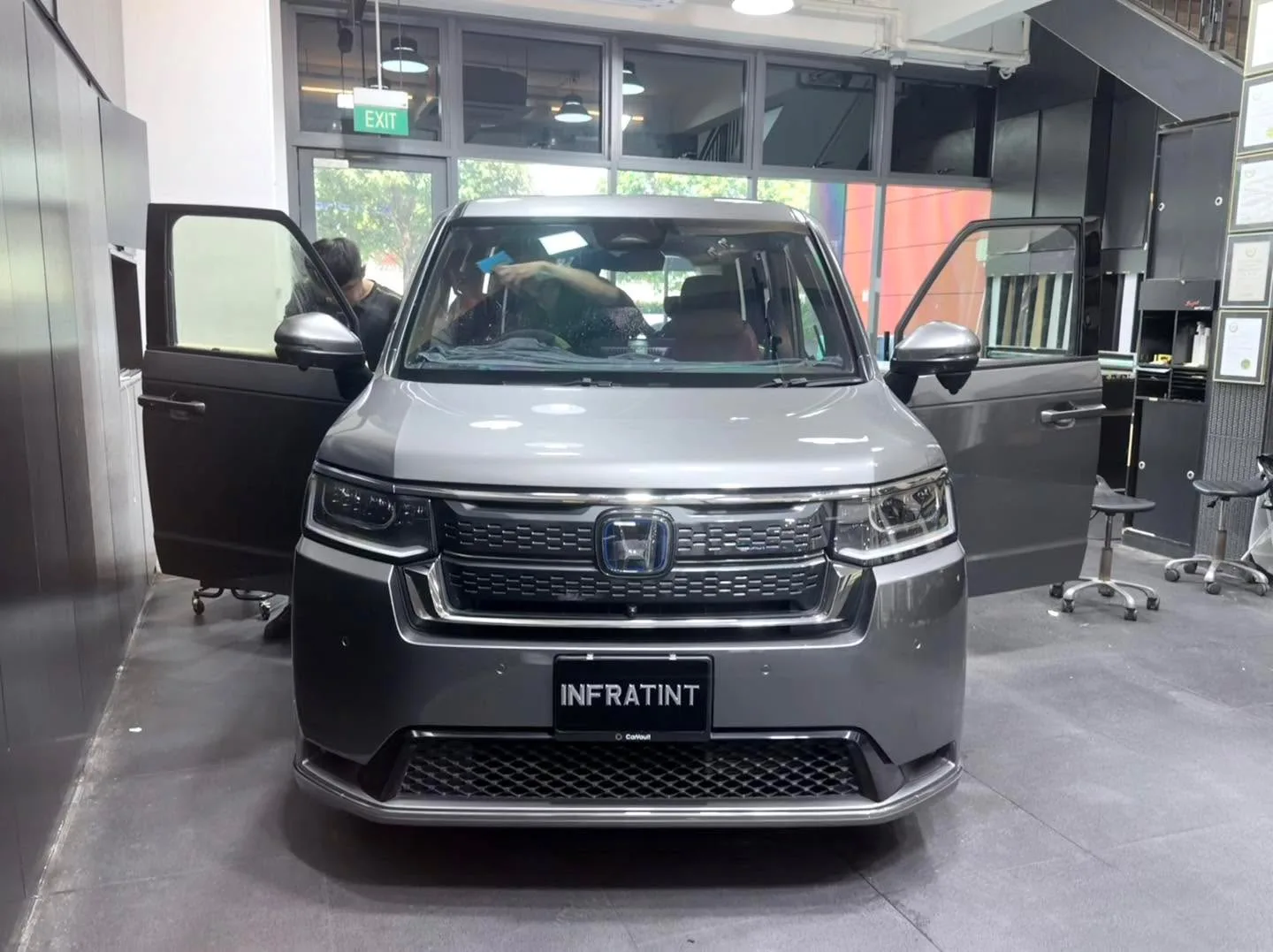 Grey Honda Spada with driver's door open, technician working on window.