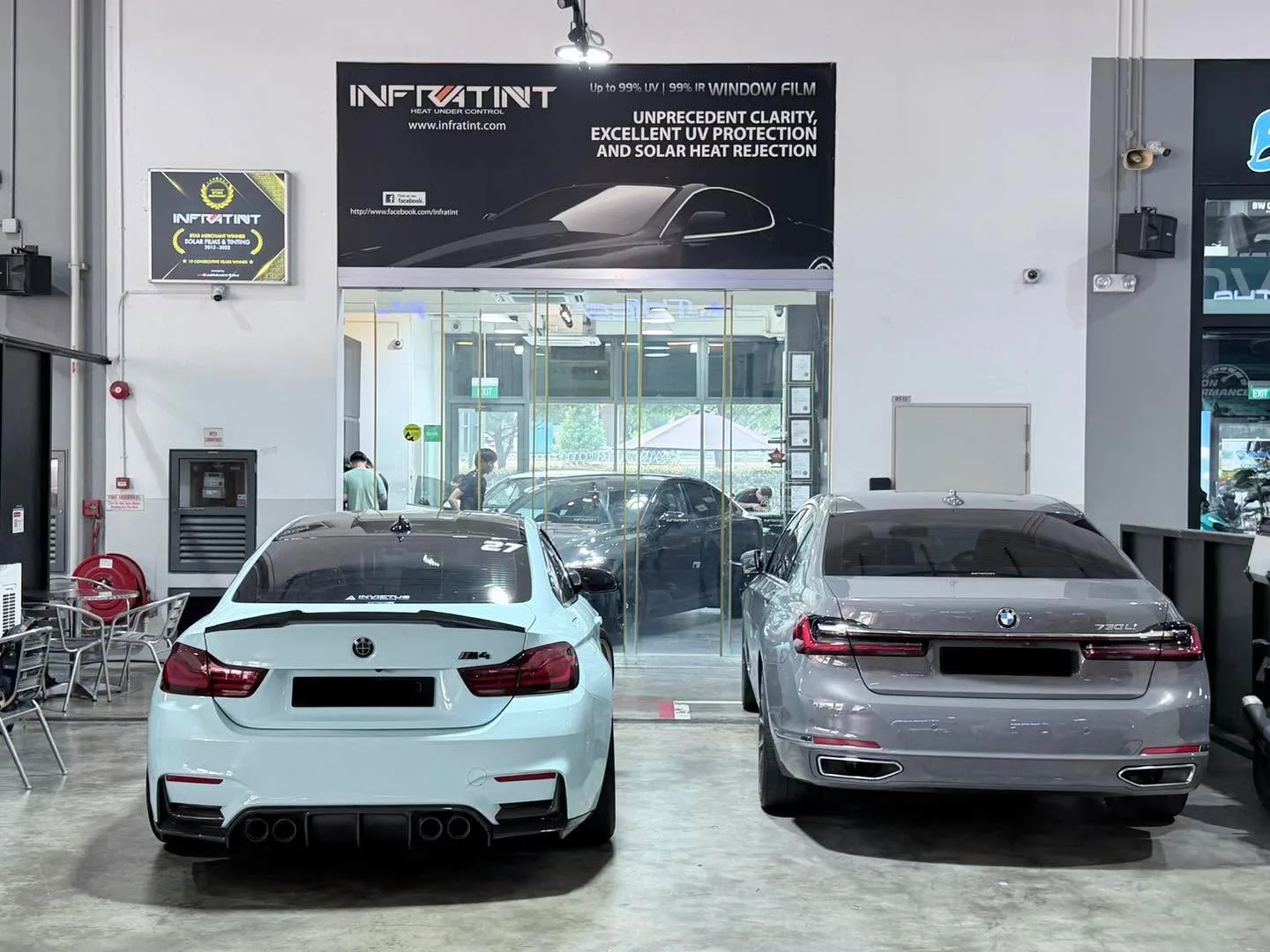 A light blue BMW M4 sedan and a grey Mercedes-Benz sedan parked in the workshop.