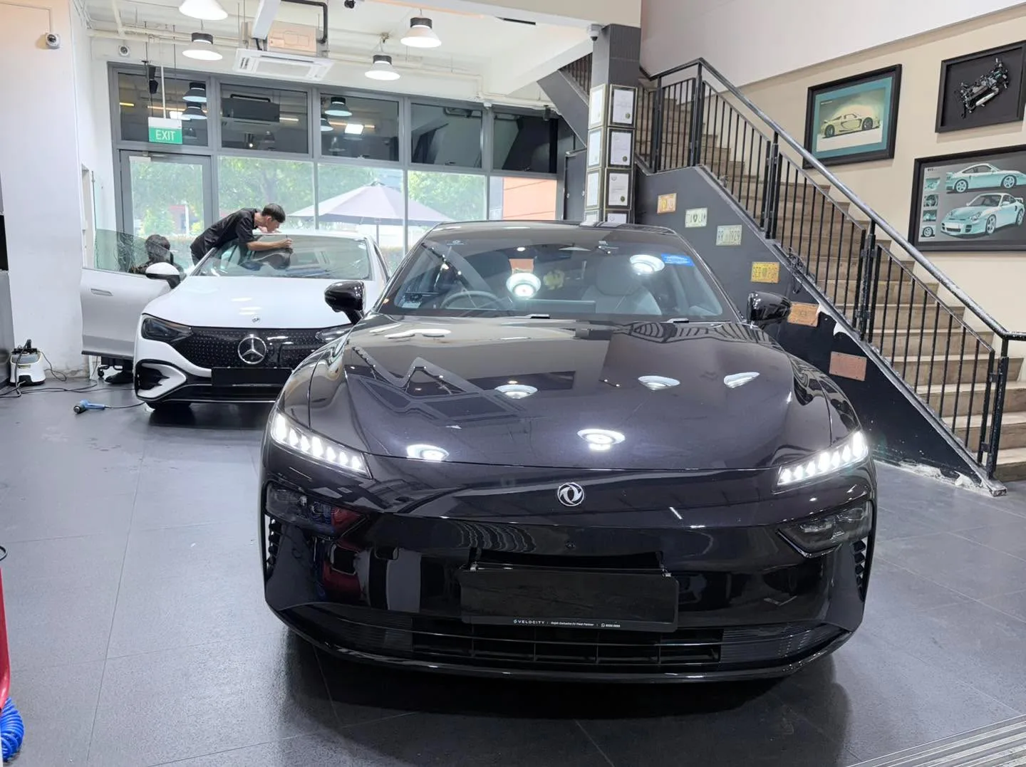 A black Dongfeng 007 sedan with LED headlights illuminated in the workshop.