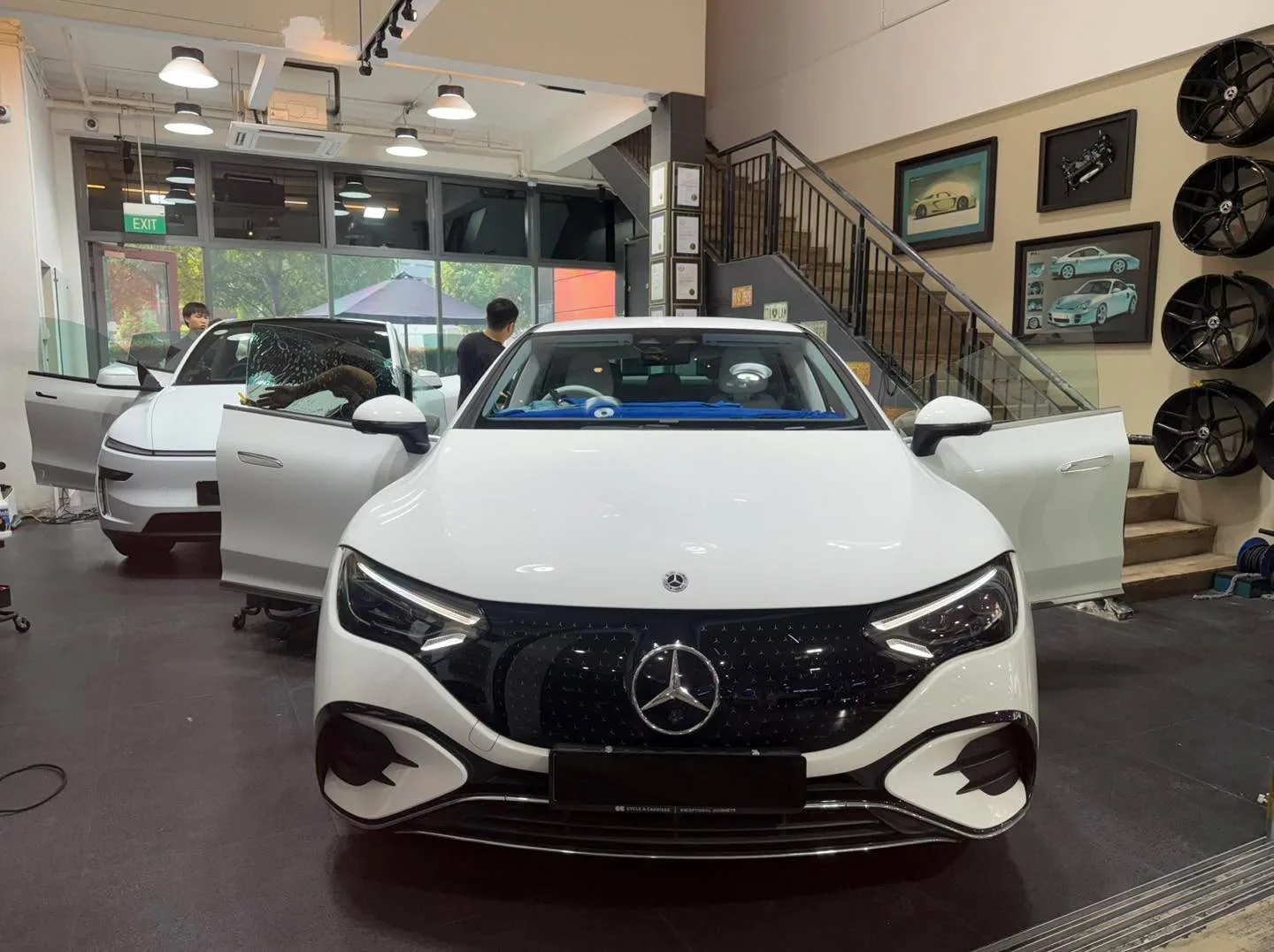 A white Mercedes-Benz EQE compact SUV with workers applying tint to the windows.