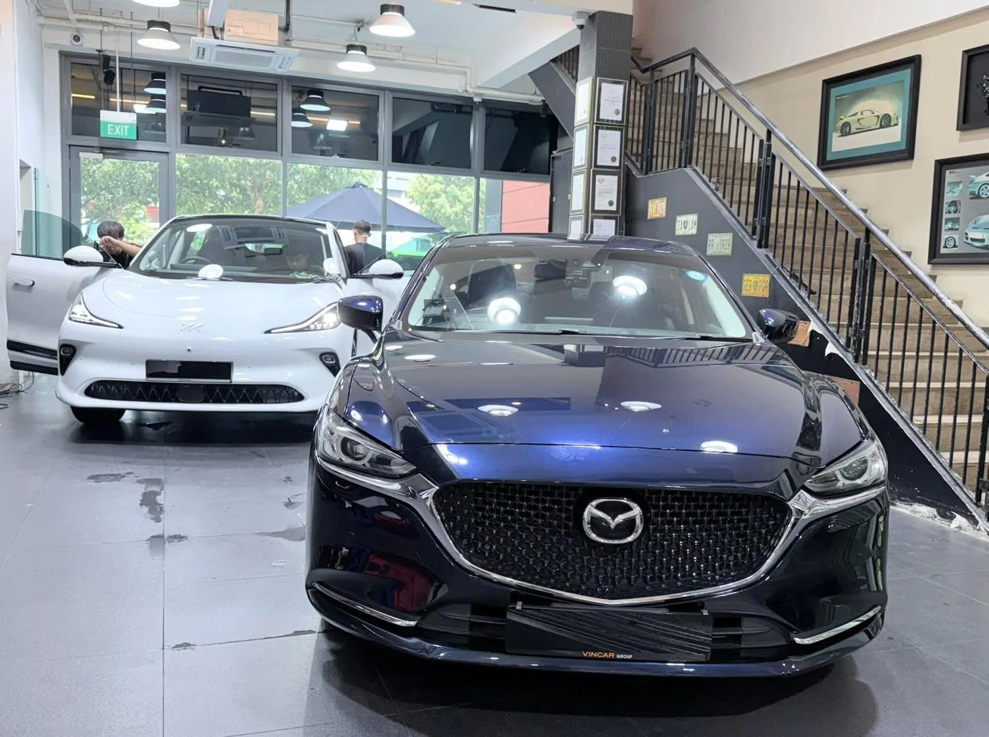 A black Mazda sedan and a white XPENG G6 SUV in the workshop with staff working.