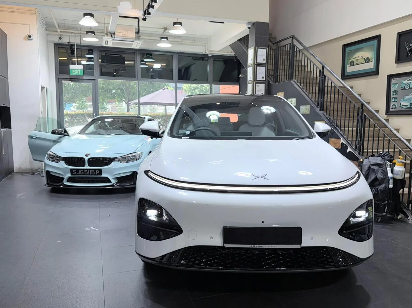 A light blue BMW M4 and white Tesla sedan with open doors during window tinting work.