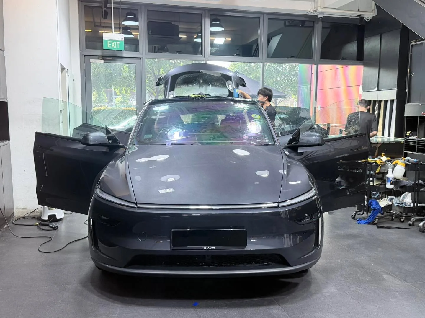 A grey Tesla sedan with open driver door undergoing window film application.