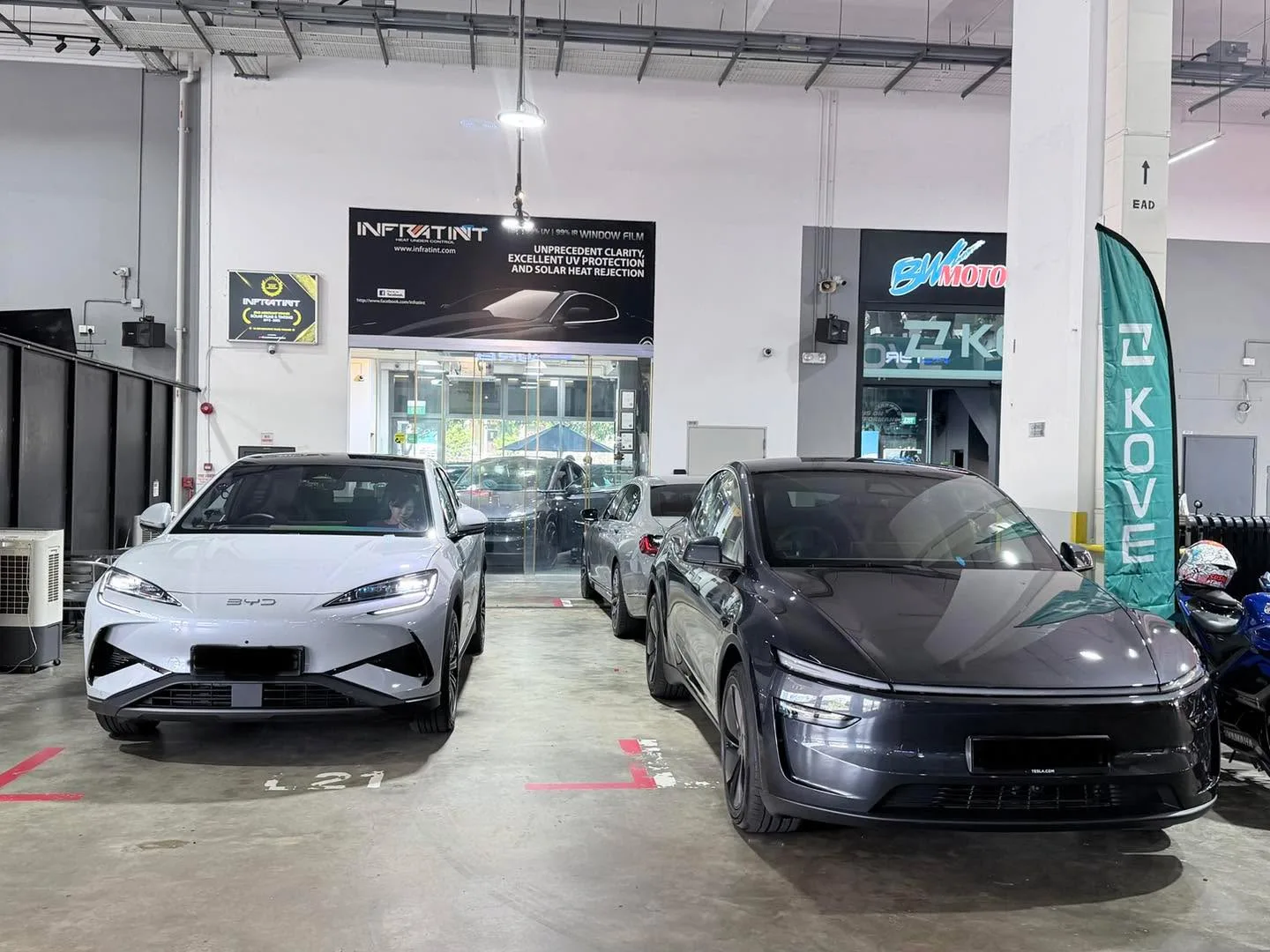 A white Tesla electric sedan and a dark grey Avatr sedan parked in the workshop alongside a black sedan.