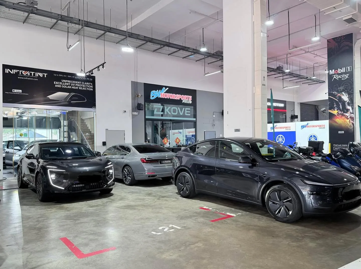 A black Avatr sedan, a silver BYD sedan, and a dark grey Tesla electric sedan parked in the workshop.