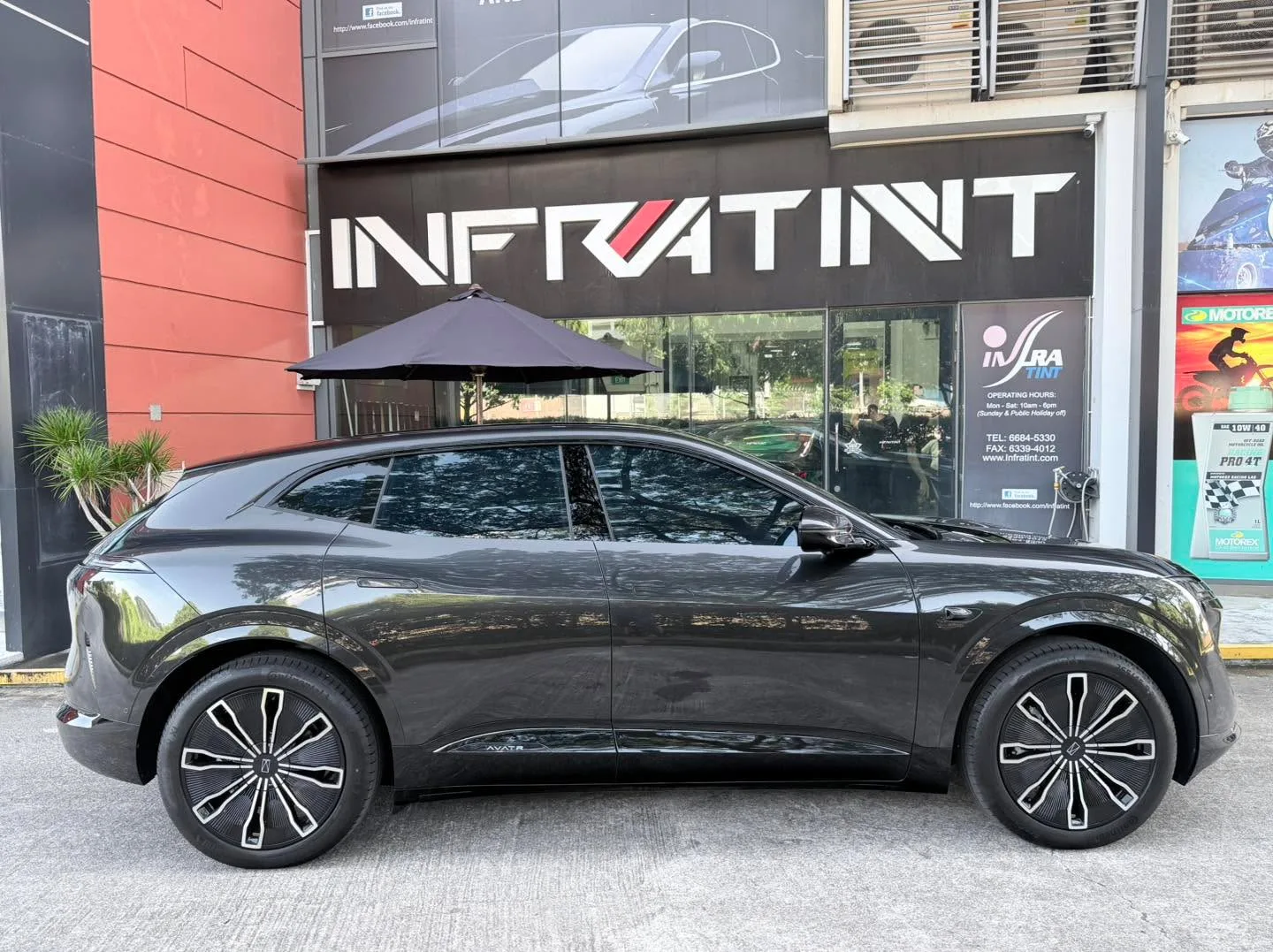 Side view of a black Avatr 07 parked outside Infratint workshop with an umbrella above.