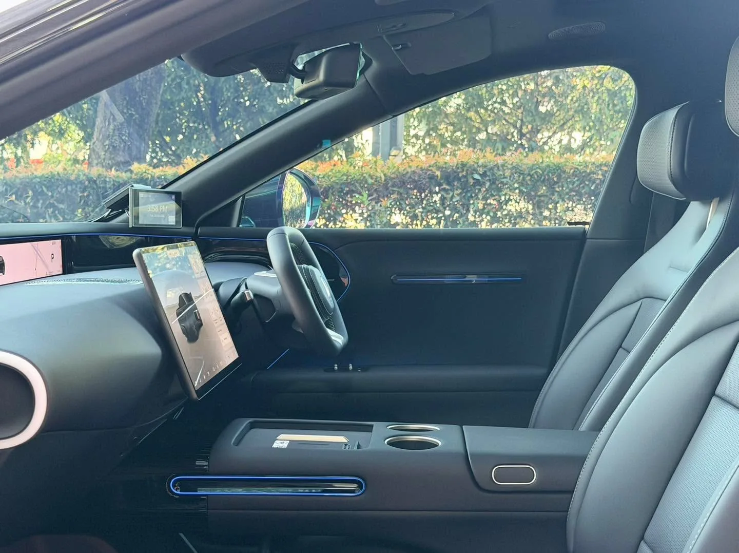 Interior view showing a dashboard and steering wheel through tinted side windows with green trees visible.