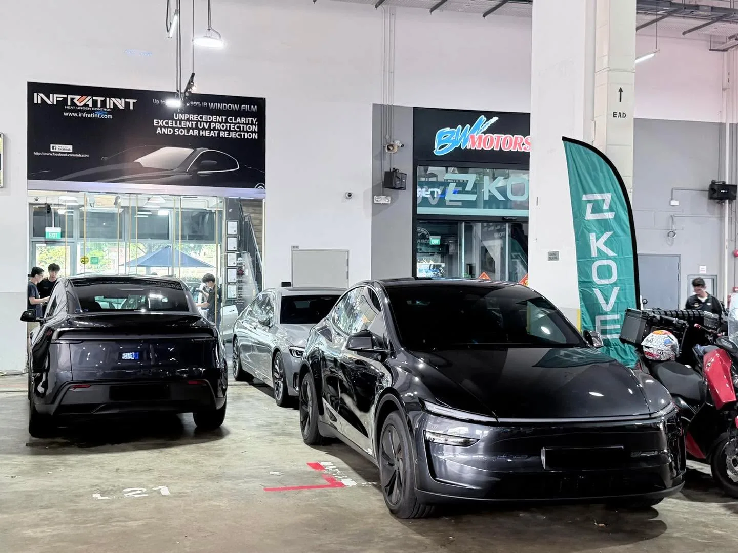 Black Tesla saloon and black electric sedan parked indoors at the workshop.