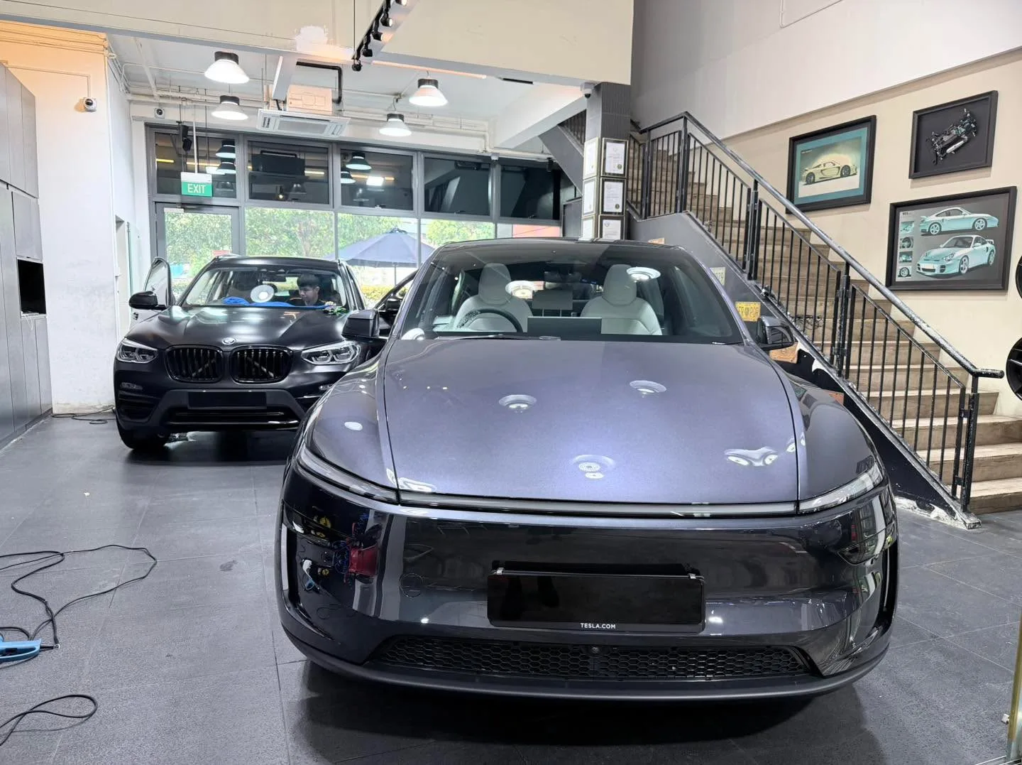 Black Tesla Model Y and black BMW X3 SUV parked indoors.