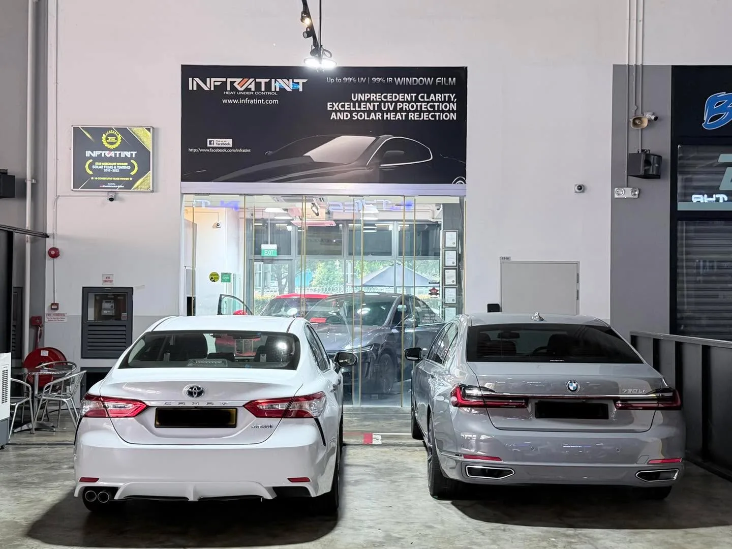 A white sedan and a grey sedan parked outside the workshop storefront.