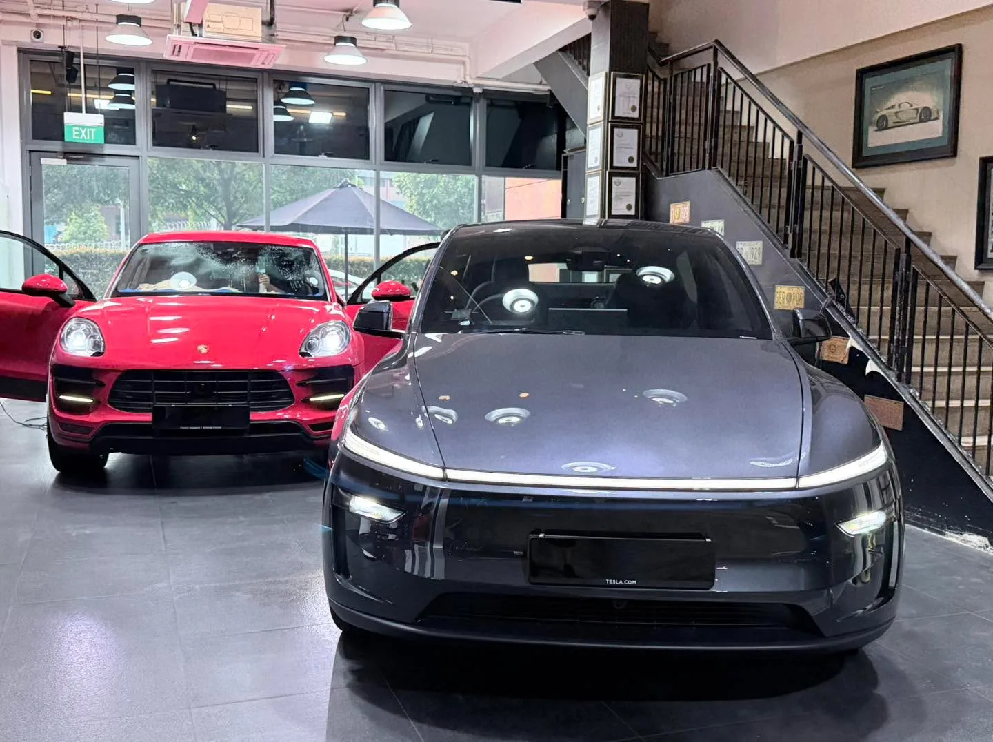 A red Porsche SUV and a grey Tesla sedan inside the workshop.
