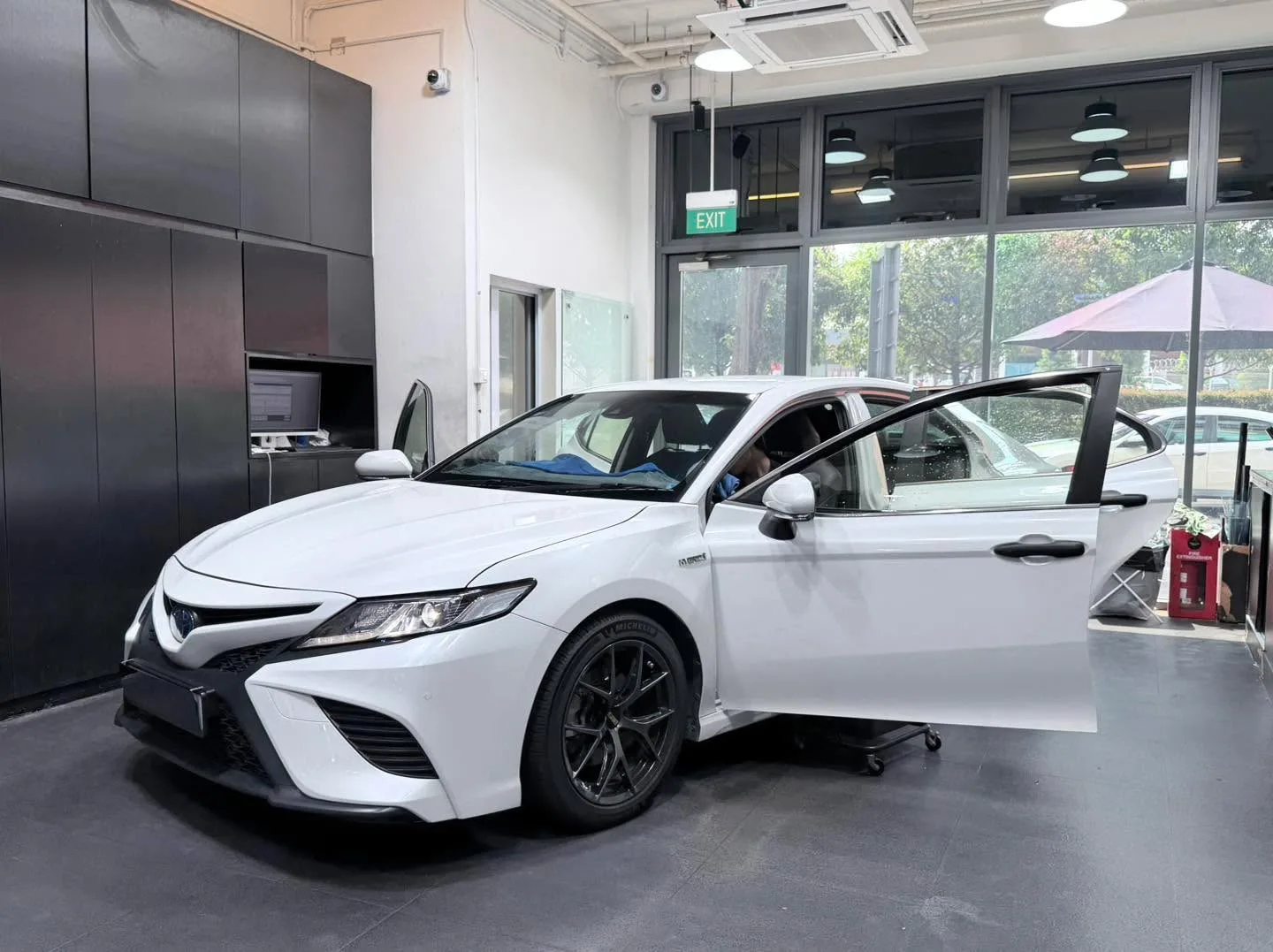 A white Toyota Camry with the driver door open in the workshop.