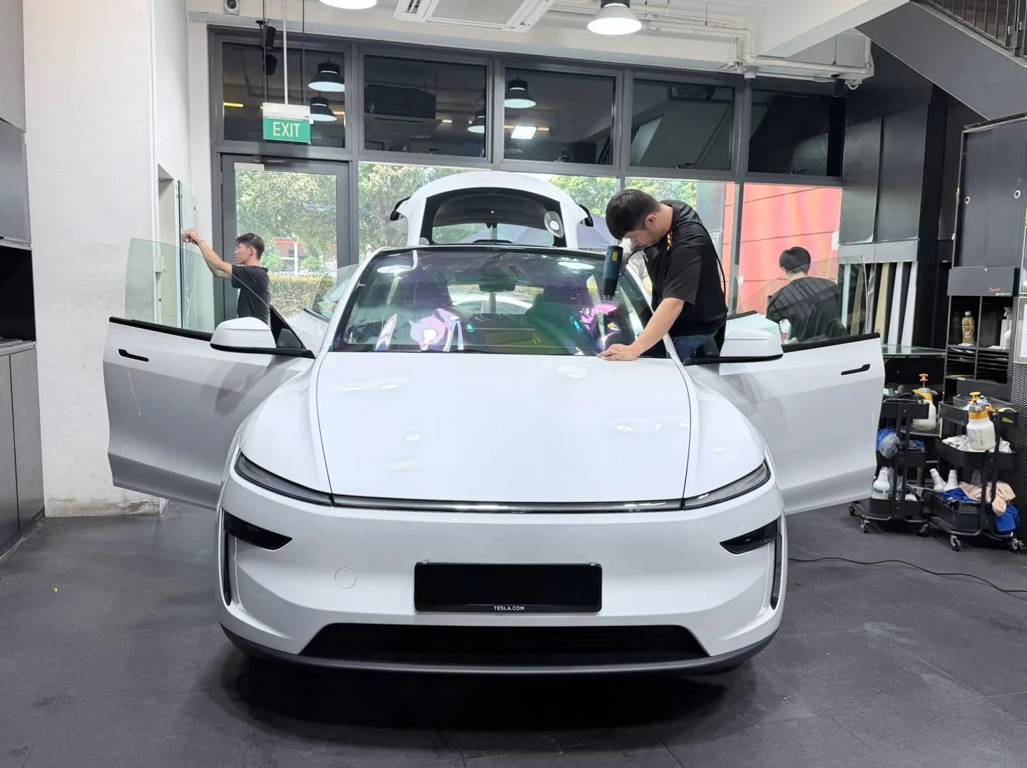 A white Tesla sedan with doors open during window tinting work.