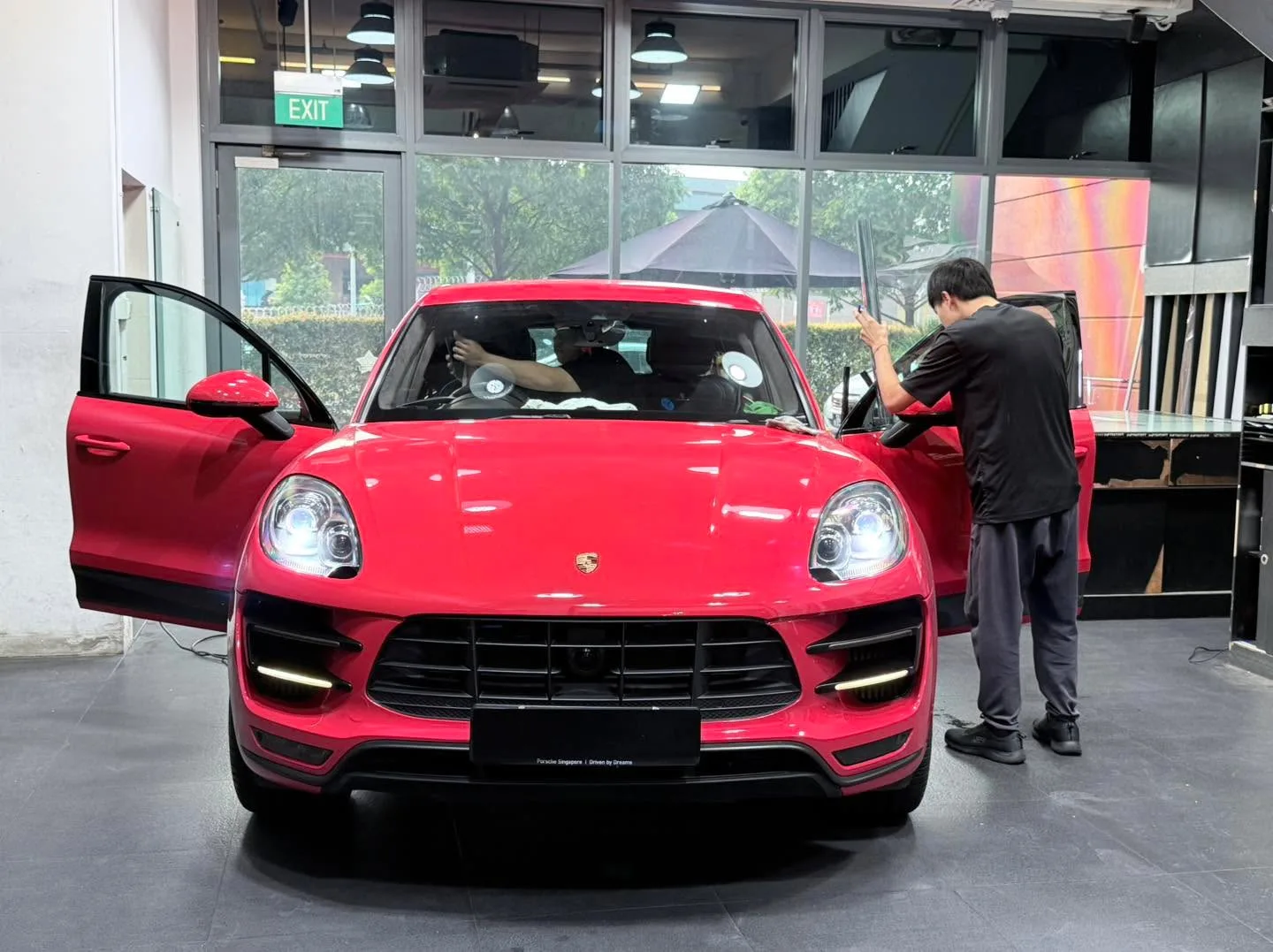 A red Porsche Macan with the door open as technician applies film.