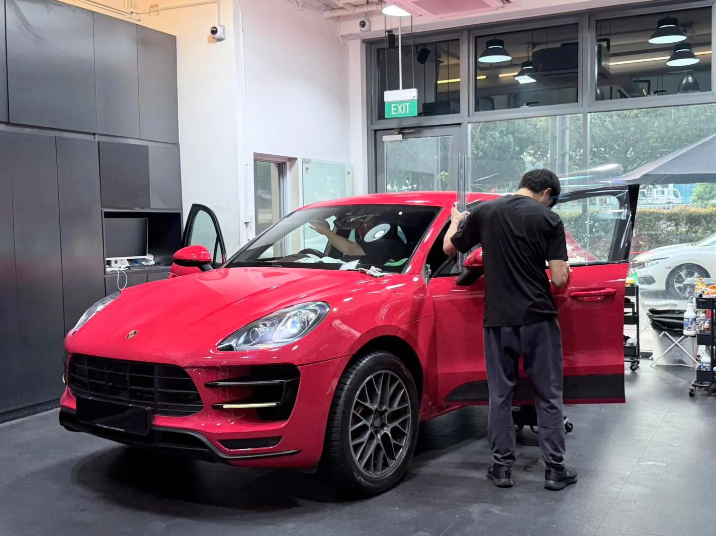 A red Porsche Macan with door open during window film installation.