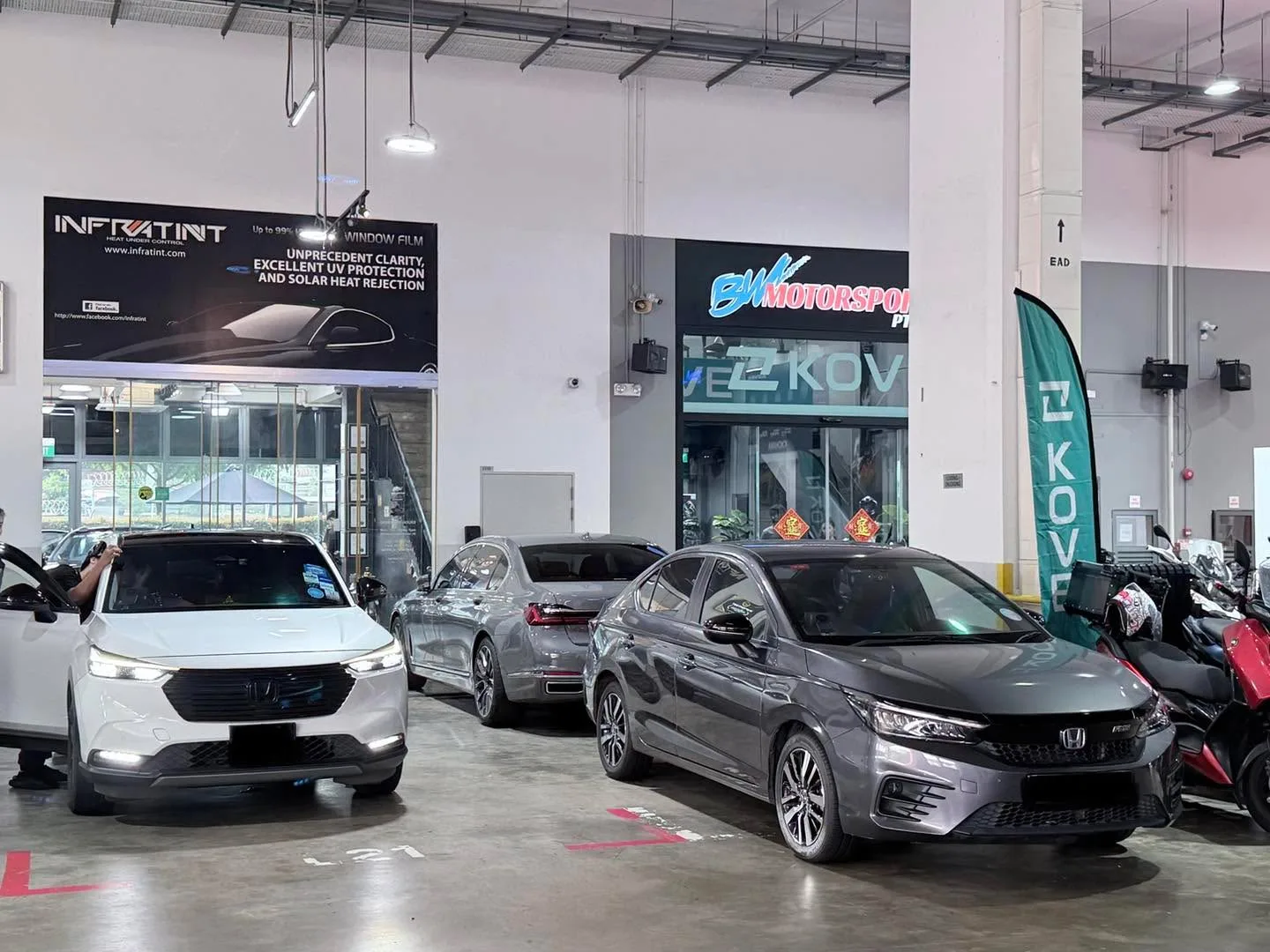 A white Honda Accord and grey Honda Vezel parked inside the workshop alongside other vehicles.